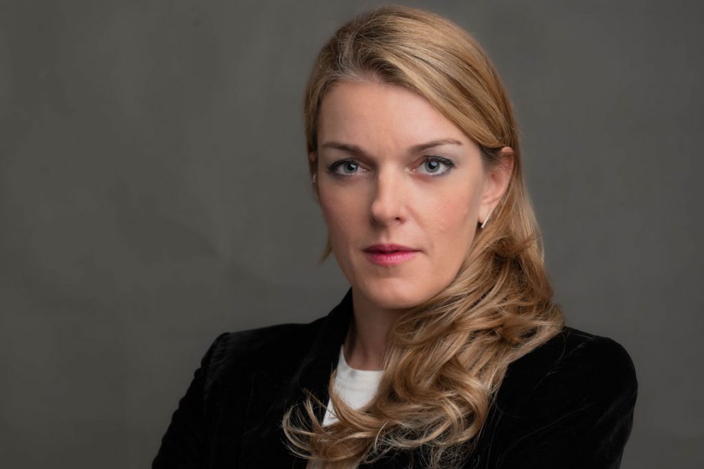 Portrait of a woman with long curly blonde hair against a plain background.