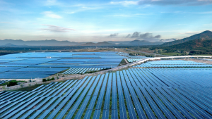 Aerial view of a vast solar farm with rows of blue solar panels and distant mountains in the background on a clear day.