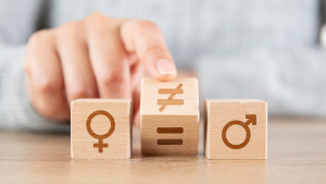 Hand pointing at wooden blocks showing the female symbol, an equality sign, and the male symbol to illustrate gender equality.